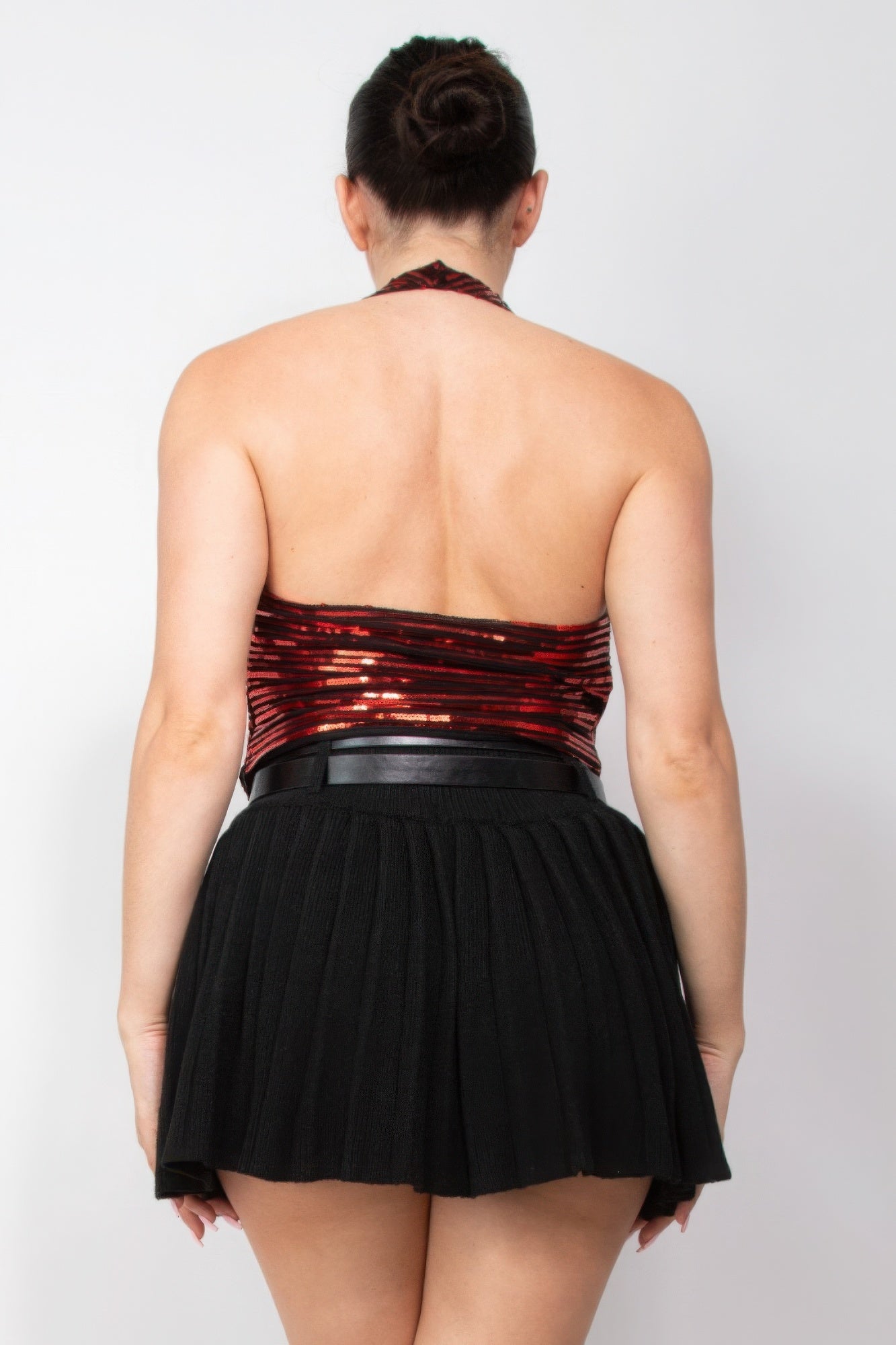 Woman wearing a dazzling Surplice Halter Sequin Top by Love It Clothing, showcasing elegance and glamour with a black pleated skirt.