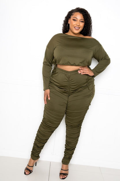 Plus size model wearing olive green off-shoulder cropped top and ruched leggings set, showcasing trendy and comfortable style.