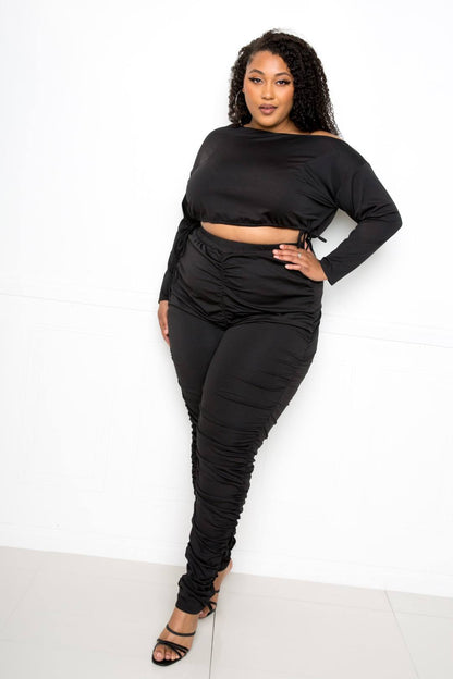 Plus size model wearing black off-shoulder cropped top and ruched leggings set, perfect for trendy and comfortable style.