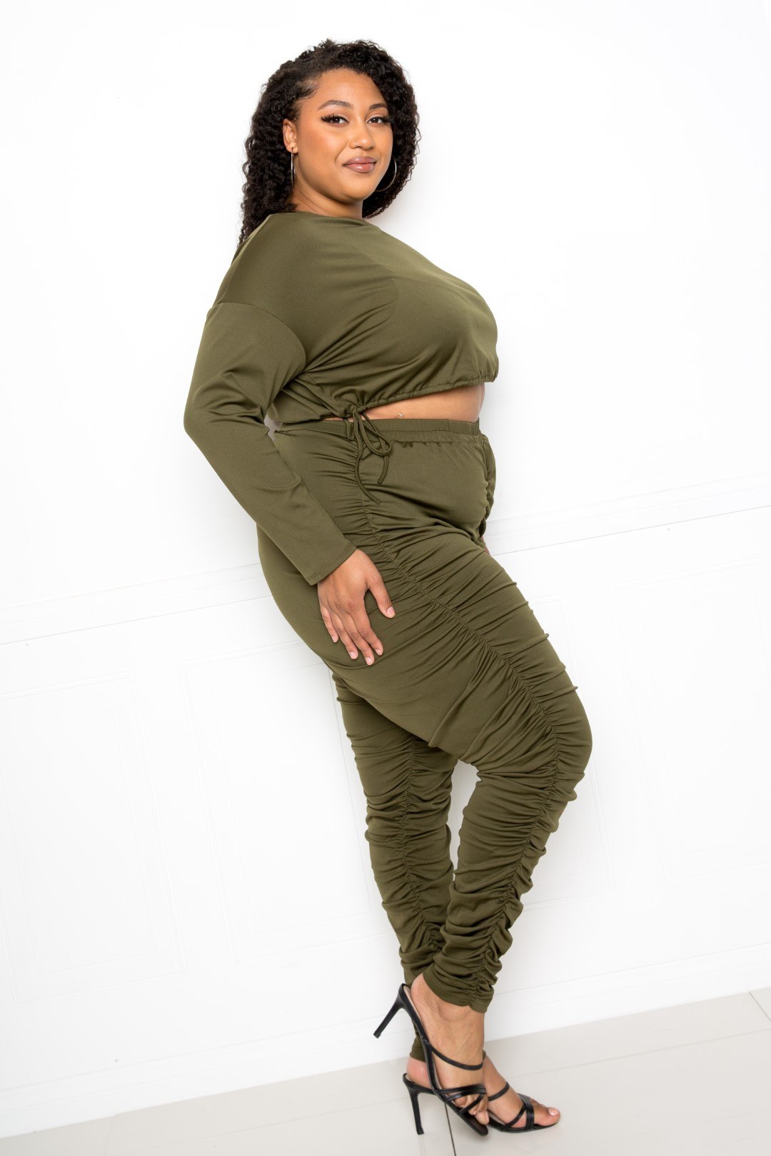 Plus-size model wearing olive off-shoulder cropped top and ruched leggings set, highlighting trendy and comfortable style.