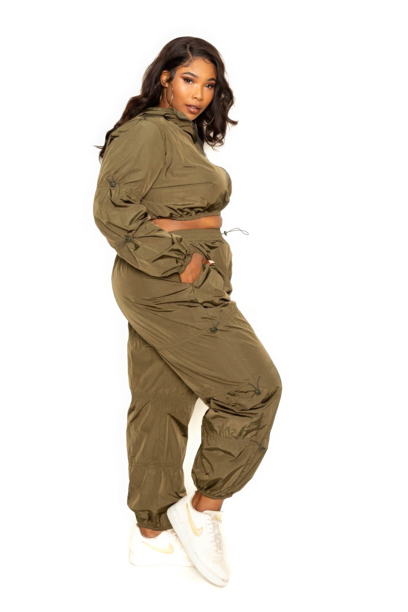 Woman in olive green active zip-up set with cord lock detail, wearing white sneakers, showcasing activewear for extended sizes.