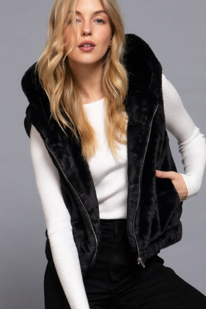 Woman wearing a black faux fur vest with hoodie by Love It Clothing, styled over a white top for a chic and cozy look.