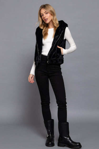 Woman wearing a black faux fur hoodie vest, styled with a white top and black pants, showcasing Love It Clothing's versatile fashion.