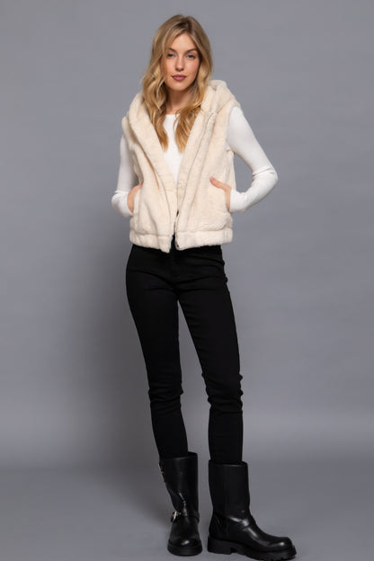 Woman wearing Vanilla Hoodie Faux Fur Vest by Love It Clothing, paired with black pants and boots, showcasing a stylish layered look.