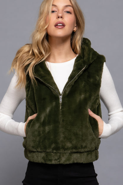 Woman wearing a dark green faux fur vest with hoodie, layered over a white top, from Love It Clothing.