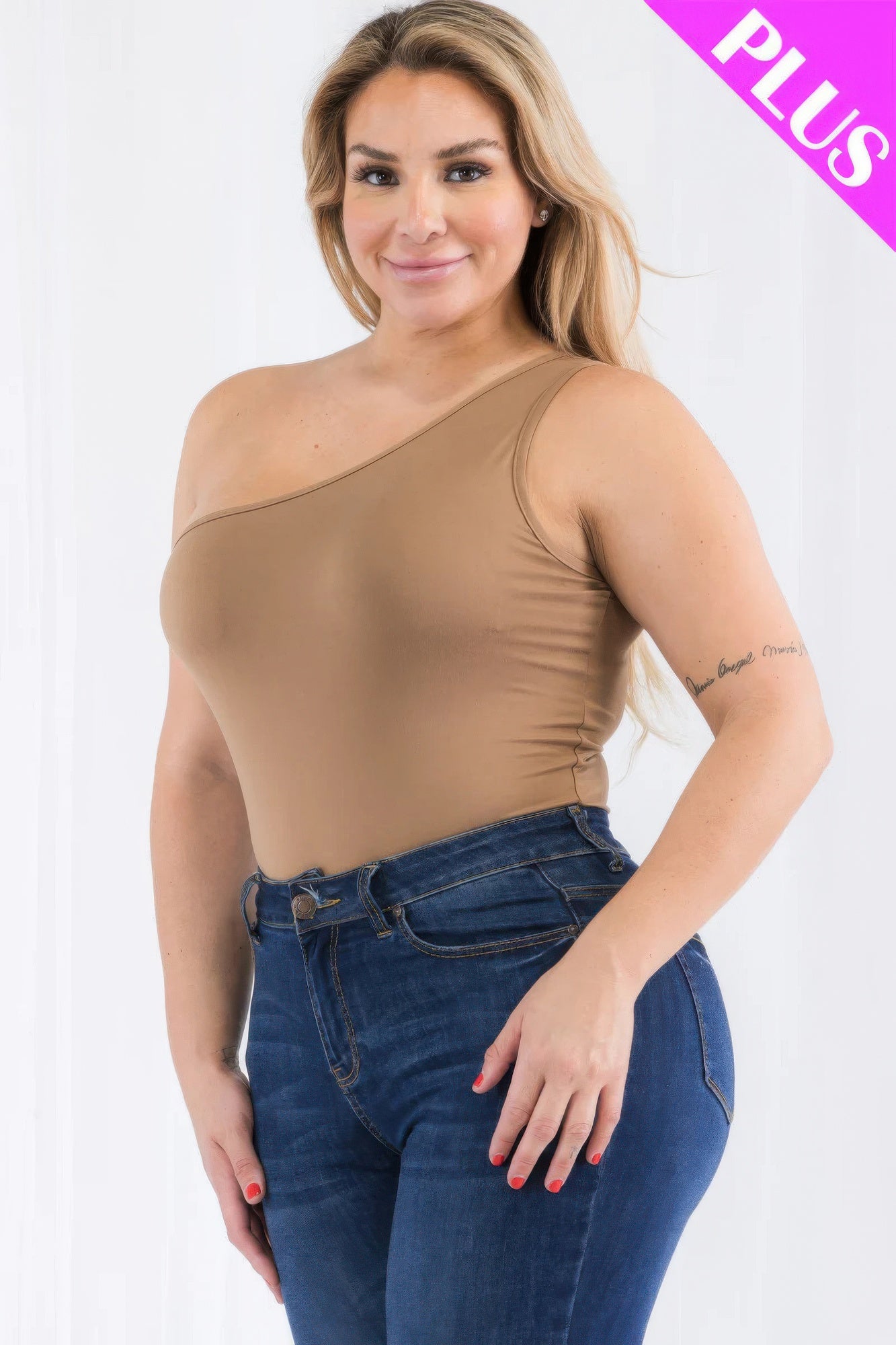 Plus size model wearing a one shoulder solid bodysuit in beige, paired with high-waisted jeans. Loveitclothing.com.