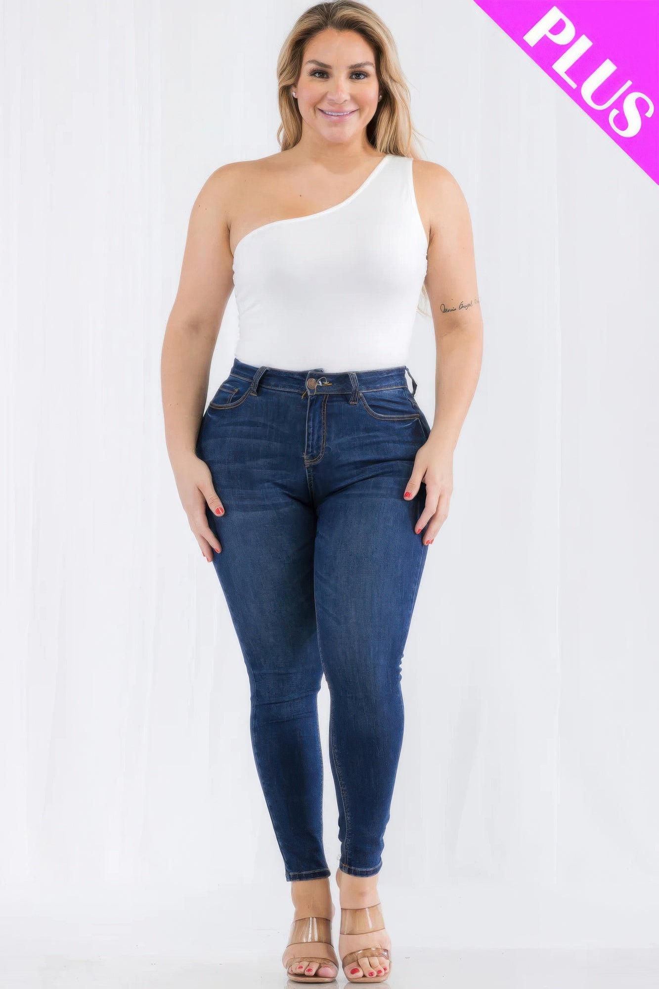 Plus size model wearing a one shoulder solid white bodysuit with dark jeans, showcasing a stylish casual look from Loveitclothing.com.